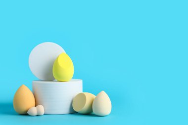 Mavi arka planda makyaj süngeri olan dekoratif podyumlar