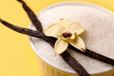 Sarı arka planda kapsüllü ve çiçekli bir kase vanilyalı şeker, yakın plan.