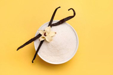 Sarı arka planda kapsüllü ve çiçekli bir kase vanilyalı şeker.