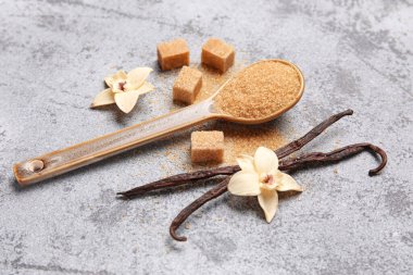 Kapsüllü ahşap kaşık vanilya şekeri ve gri arka planda çiçekler, yakın plan.