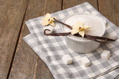 Kapsüllü vanilya şekeri ve ahşap arka planda çiçekler, yakın plan.