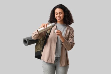 Beyaz arka planda termos ve sırt çantalı genç Afro-Amerikalı bayan turist