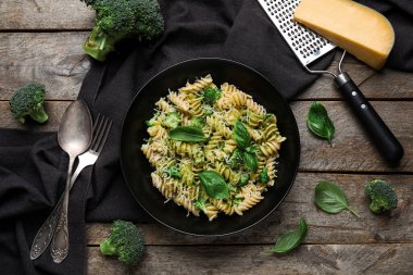 Bir kase lezzetli fusilli makarna brokoli ve ahşap zemin üzerinde fesleğen yaprakları.
