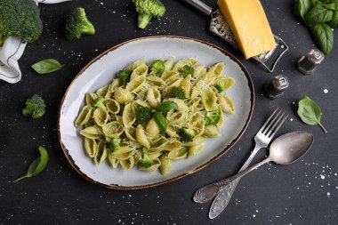 Brokoli ve siyah arka planda fesleğen yapraklı lezzetli koni rigli makarna tabağı.