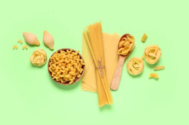 Ahşap kâse ve kaşık ile kompozisyonda yeşil arka planda farklı türde çiğ makarna.