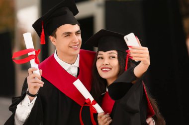 Diplomalı birkaç öğrenci üniversitenin yanında selfie çekiyorlar.