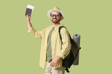 Yeşil arka planda pasaportu ve sırt çantası olan genç bir erkek turist.