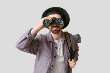 Sırt çantalı genç bir turist gri arka planda dürbünle bakıyor.