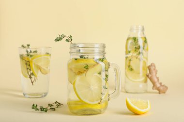 Mason kavanozu ve bir bardak taze limon karışımı zencefil ve kekik katılmış sarı arka planda.