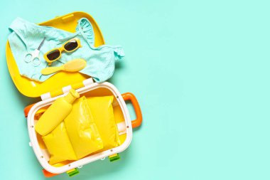 Çocuk kıyafetleri ve turkuaz arka planda banyo aksesuarları.