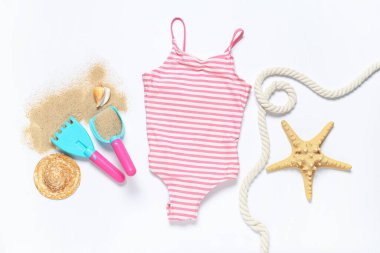 Beyaz arka planda çocuk mayosu, ip, kum, oyuncak tırmık ve kürekle kompozisyon