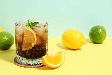 Bir bardak Long Island buzlu çay kokteyli. Nane ve turkuaz arka planda sarı masada farklı narenciye meyveleri.