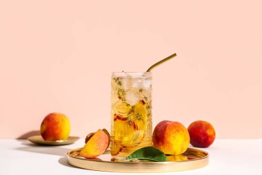 Bir bardak taze şeftalili limonata kekik ve bej arka planda beyaz masada meyveler.