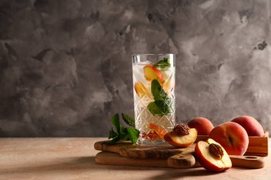 Bir bardak taze şeftalili limonata, nane ve bej masada meyveler.