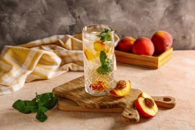 Bir bardak taze şeftalili limonata, nane ve bej masada meyveler.