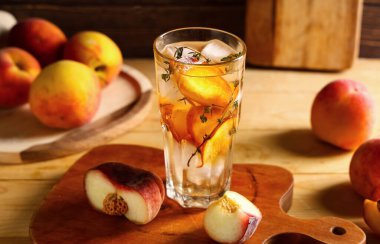 Bir bardak taze şeftalili limonata kekik ve ahşap arka planda meyveler.