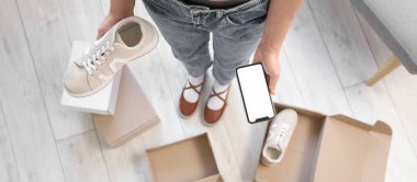 Cep telefonlu genç bir kadın dükkanda yeni ayakkabılar seçiyor.