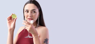 Açık arkaplanda bir bardak martini ve metin için yeri olan güzel genç bir kadın.