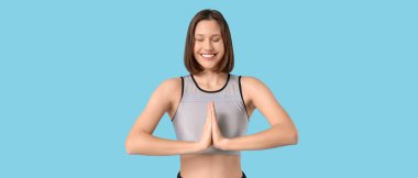 Sportif genç kadın mavi arka planda meditasyon yapıyor.