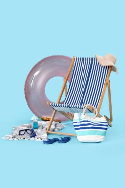 Güverte sandalyesi, şişirilebilir yüzük ve mavi arka planda bir bardak kokteyl.