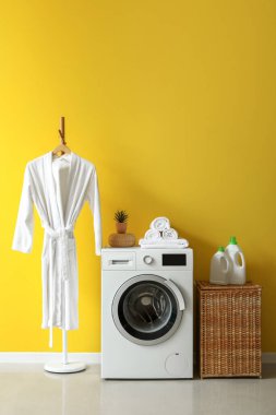 Çamaşır odasının içinde hasır sepeti, çamaşır makinesi ve bornoz var.