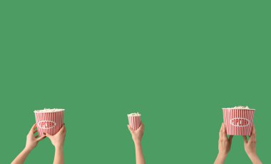 Hands holding buckets with popcorn on green background