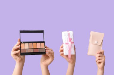 Göz falı olan kadın elleri, hediye kutusu ve leylak arka plandaki fırçalar için çanta.