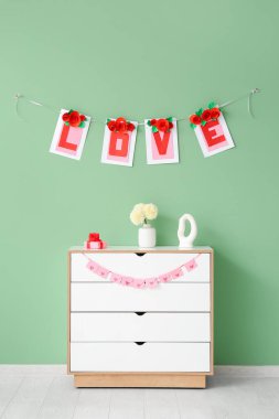 Çekmecelerin üzerinde hediye kutuları ve yeşil duvarın yanında aşk sözcüğü var. Sevgililer Günü kutlaması