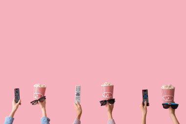 Kovalarca patlamış mısır, 3 boyutlu gözlük ve pembe arka planda televizyon kumandalı eller.