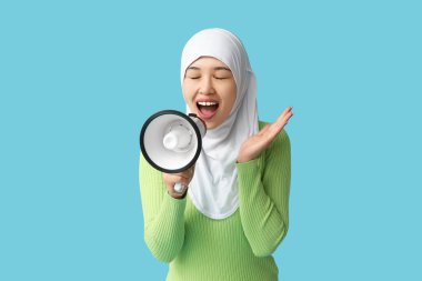 Genç Asyalı Müslüman kadın mavi arka planda megafona bağırıyor. Ulusal Duyulma Günü