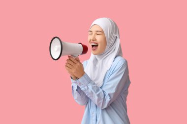 Genç Asyalı Müslüman kadın pembe arka planda megafona bağırıyor. Ulusal Duyulma Günü
