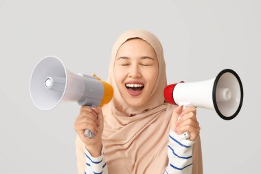 Genç Asyalı Müslüman kadın gri arka planda megafona bağırıyor. Ulusal Duyulma Günü