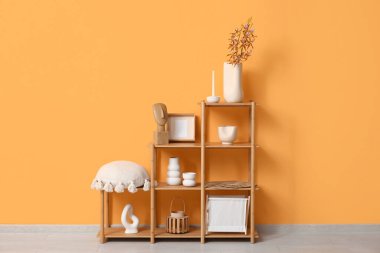 Oturma odasındaki turuncu duvarın yanında yastıklı, heykelcikli ve vazolu raf ünitesi.