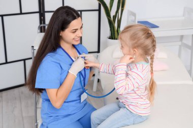 Steteskoplu küçük kız klinikteki çocuk doktorunu dinliyor.