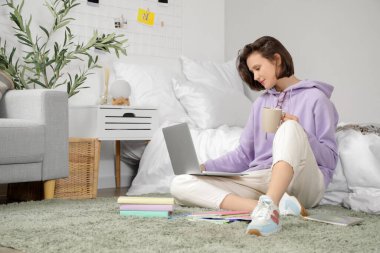 Güzel öğrenci yatak odasında dizüstü bilgisayarla ders çalışıyor.