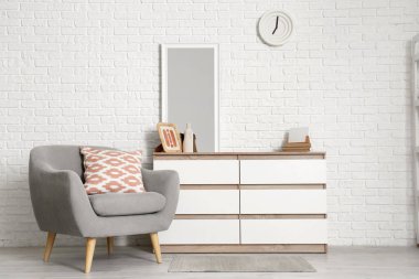 Oturma odasındaki beyaz tuğla duvarın yanında aynalı çekmeceler ve koltuklar.