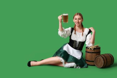 Güzel mutlu Ekim Festivali garsonu, fıçılar ve kupa birayla yeşil arka planda oturuyor.
