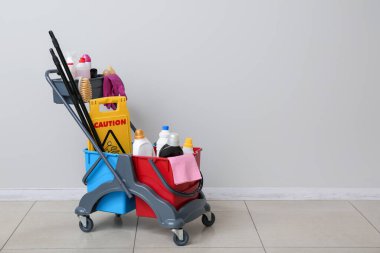 Gri duvarın yanında temizlik malzemeleri var.