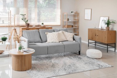 Pencerenin yanında gri kanepe ve sehpası olan şık bir oturma odası.