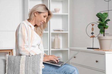 Evdeki kanepede dizüstü bilgisayar kullanan olgun bir kadın.