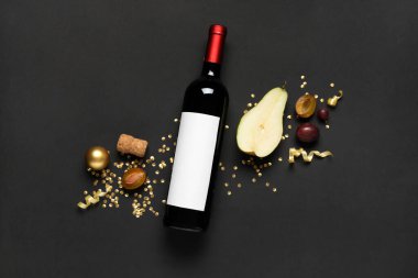 Bir şişe şarap, meyve, konfeti ve siyah arka planda yılan yağı.