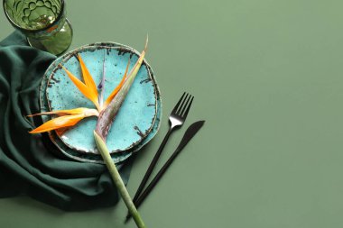 Yeşil arka planda güzel strelitzia çiçeği, çatal bıçak takımı ve peçeteli tabaklar.