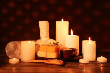 Mumları havluyla yakmak, bitkisel çanta, sabun barları ve ahşap masada koyu arka planda bir kase fırça.