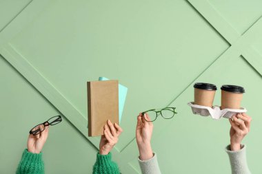 Gözlüklü, kitaplı ve yeşil arka planda kahve fincanı olan kadın eller.