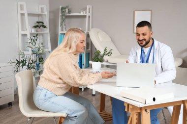 Klinikteki masada dizüstü bilgisayar kullanan olgun bir kadın olan erkek doktor.