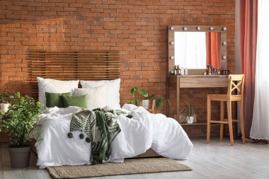 Yatak odasının içindeki tuğla duvarın yanında ahşap tuvalet masası ve yatak.