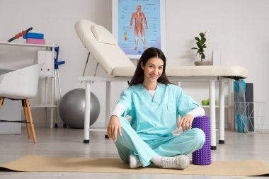 Rehabilitasyon merkezinde köpük silindirli kadın fizyoterapist.