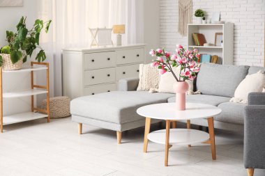 Konforlu kanepe ve çiçek açan manolya dalları oturma odasının içindeki sehpanın üzerindeki vazoda.