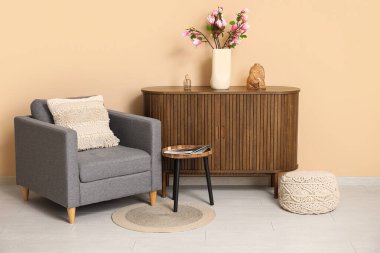 Oturma odasındaki şık koltuğun yanındaki çekmecelerde çiçek açan vazo.