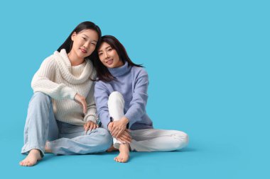 Güzel, mutlu Asyalı kız kardeşler mavi arka planda oturuyor.